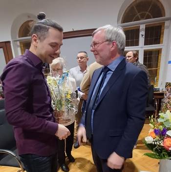 Das Foto zeigt zwei Personen im Sitzungssaal des Luckenwalder Rathauses, die linke Person überreicht Blumen an die rechte Person.