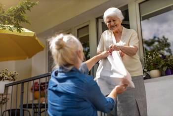 Das Bild zeigt eine Frau, die einer älteren Dame eine Tüte reicht.