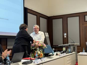 Das Foto zeigt zwei Personen im Sitzungssaal des Rathauses Luckenwalde mit Blumensträußen.