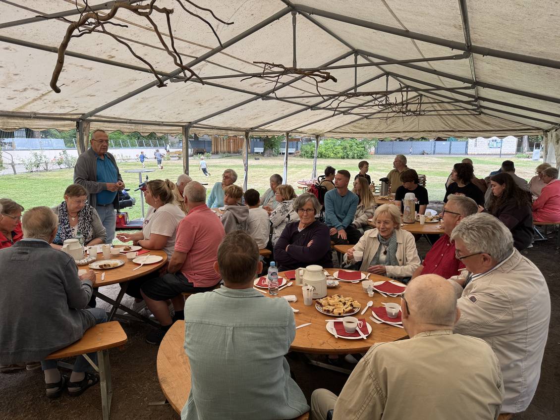 Das Foto zeigt viele Menschen unter einem Zelt, die einem Mann zuhören.
