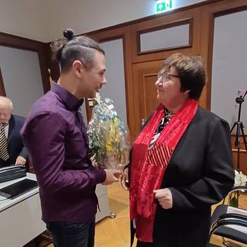 Das Foto zeigt zwei Personen im Sitzungssaal des Luckenwalder Rathauses, die linke Person überreicht Blumen an die rechte Person.